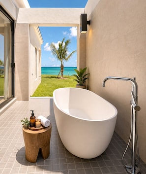 A modern bathroom with a freestanding bathtub, a shower, and a view of a tropical landscape.