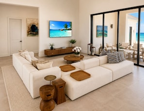 A modern living room with a large sofa, wooden side tables, a coffee table, and a TV mounted on the wall. - Casa Mar Bimini Beach Villa – Rockwell (North Bimini)