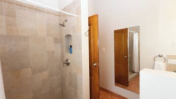 A bathroom with a shower, a wooden door, a mirror, and a white sink.