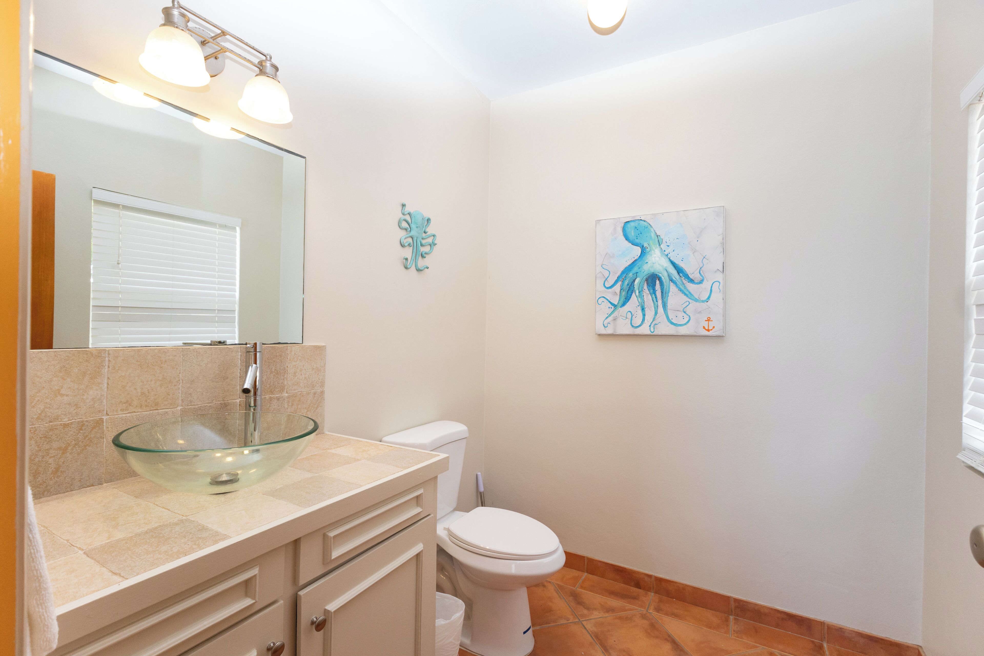 A bathroom with a glass bowl sink, white toilet, and a painting of an octopus on the wall.