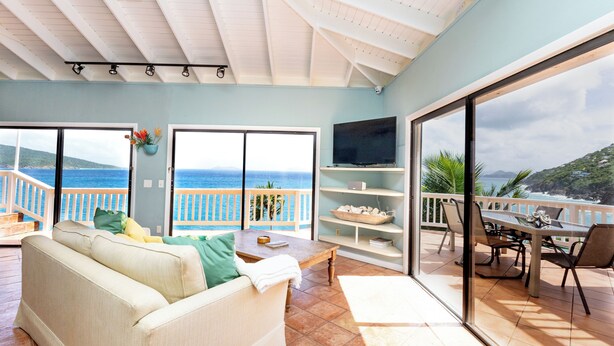 A spacious living area with a sofa, dining table, and chairs, overlooking a scenic ocean view. - The Breeze (ST Thomas)