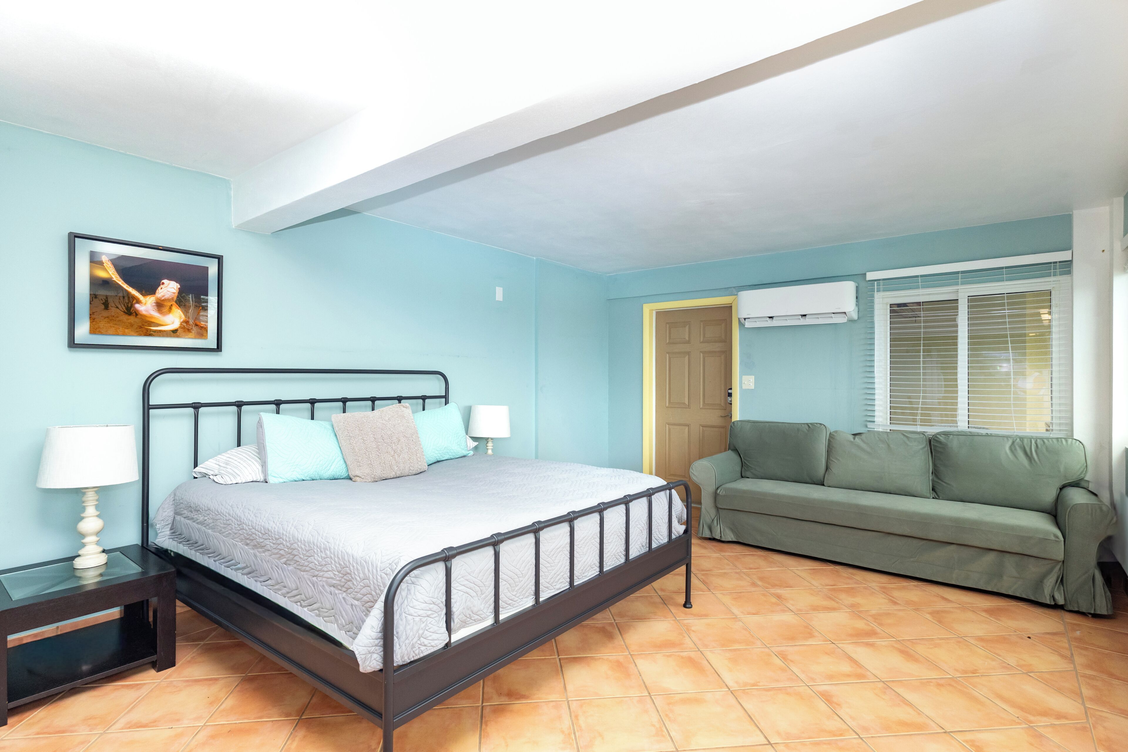 Une chambre à coucher avec un lit, une table de chevet, un canapé vert et un tableau au mur.