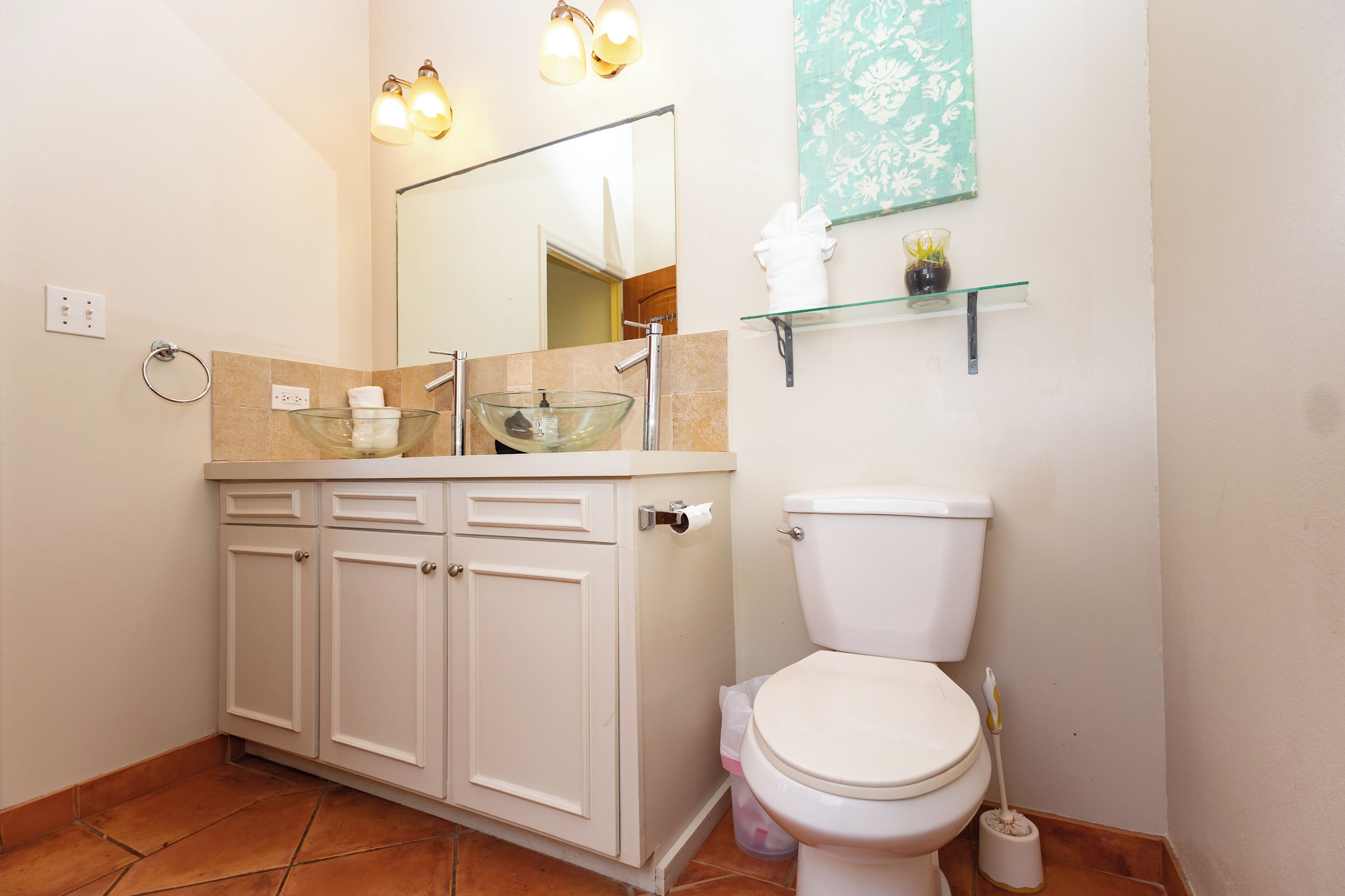 A bathroom with a glass sink, white toilet, and a mirror above the sink.