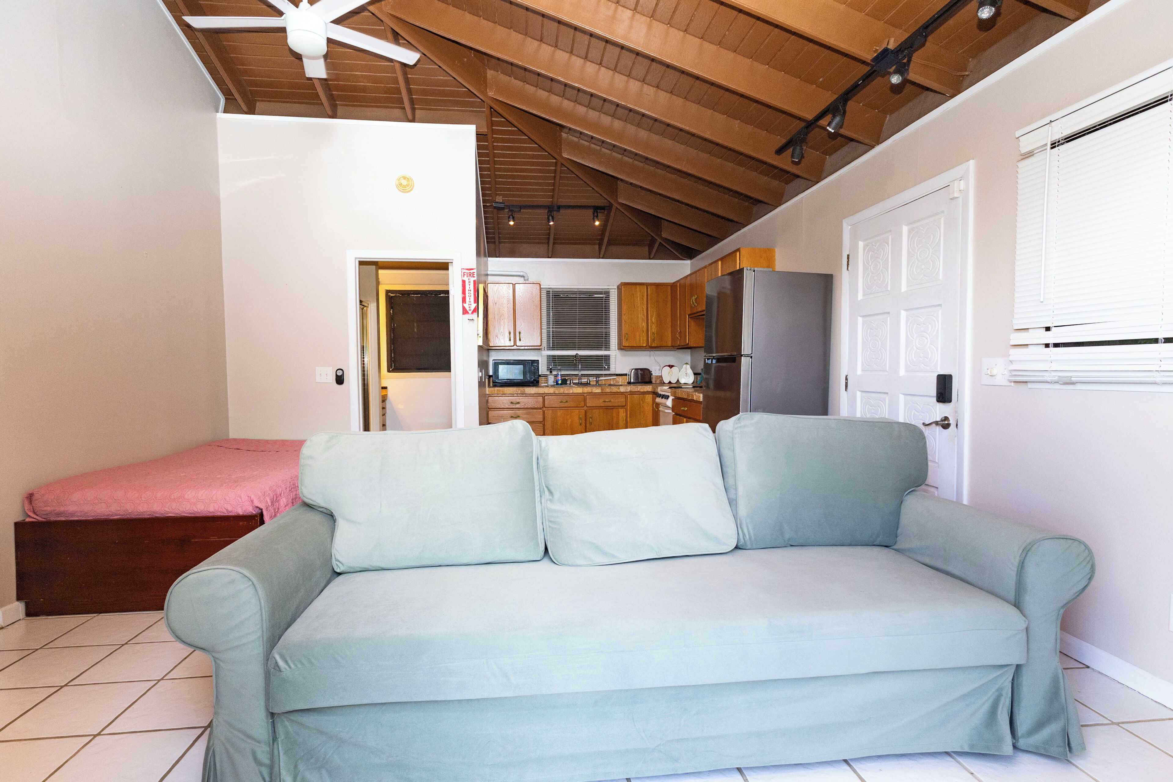 A living room with a sofa, a bed, and a kitchen in the background.