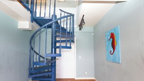 A blue spiral staircase in a room with light blue walls and a red seahorse painting. - The Breeze (ST Thomas)