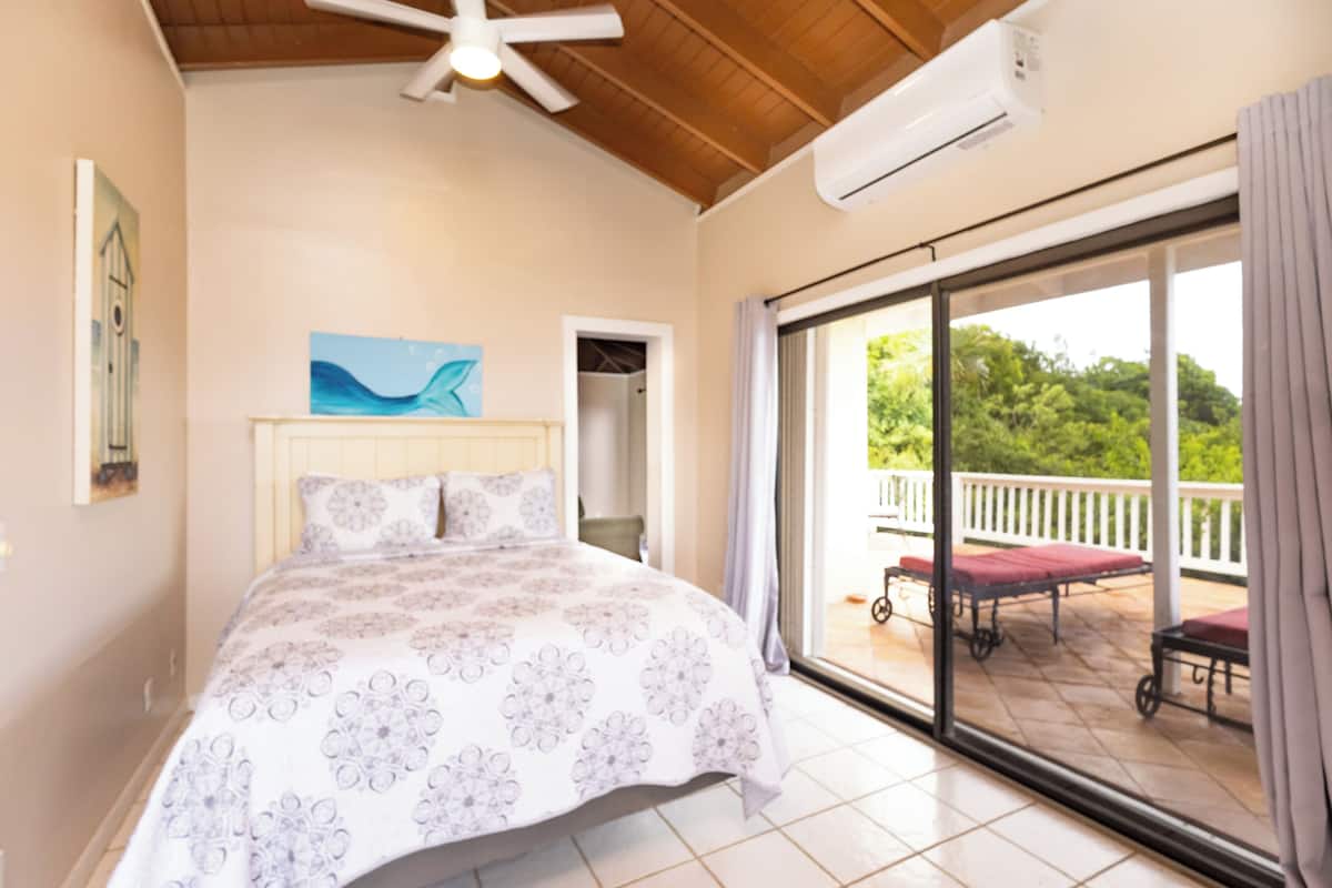 A bedroom with a bed, a ceiling fan, an air conditioning unit, a sliding glass door leading to an outdoor area with a patio table and chairs.