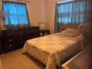 Ein Schlafzimmer mit Bett, Schminktisch, Nachttisch, Lampe und Vorhängen.