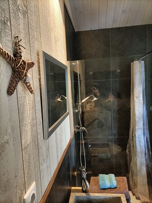 Une salle de bain avec un meuble-lavabo en bois, une dĂ©coration en forme dâĂ©toile de mer, un miroir, une douche avec une porte en verre et une serviette posĂ©e sur un tabouret.