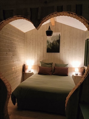 A cozy room with a bed, two nightstands, a hanging light, and a painting on the wall.