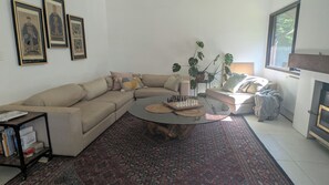 Ein Wohnzimmer mit einem beigefarbenen Sofa, einem Couchtisch, einem Bücherregal und gerahmten Kunstwerken an der Wand.