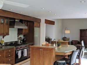 Eine moderne Küche mit Holzschränken, einer Granit Arbeitsplatte, einem eingebauten Herd und einer zentralen Kochinsel mit Sitzgelegenheit.