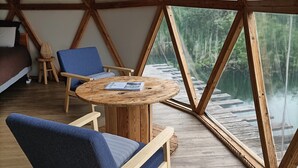 Une pièce dotée d’une structure de plafond en bois, d’une table ronde en bois, de deux chaises bleues et offrant une vue sur une forêt grâce à de grandes fenêtres.