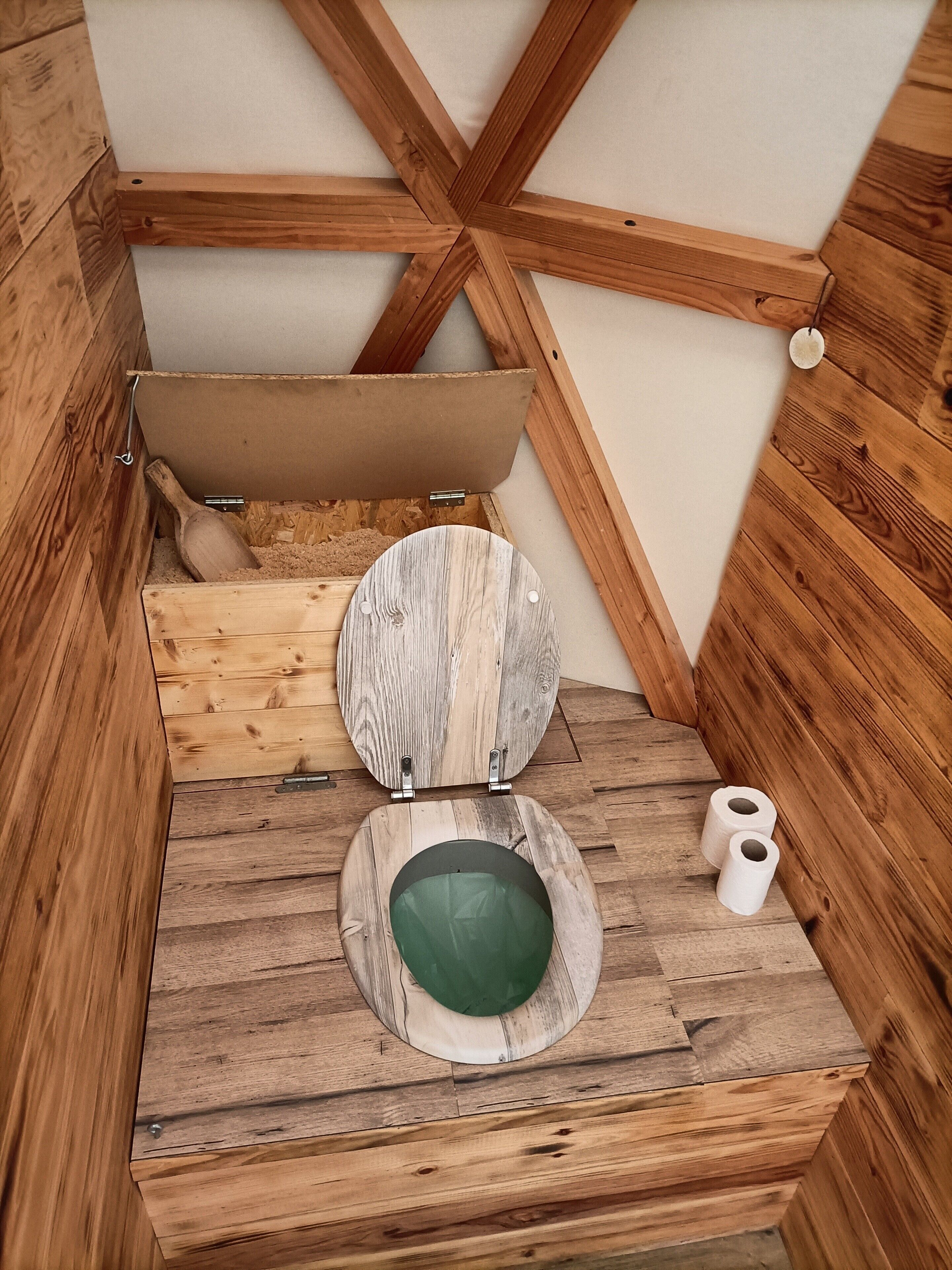 A wooden toilet with a rustic design, a wooden seat, and a green bowl.