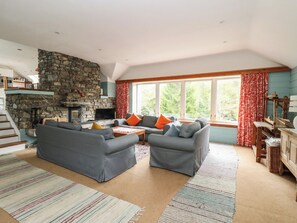 A living room with a stone fireplace, grey sofas, a television, and a large window with curtains. - Culearn Mill (Lochearnhead)