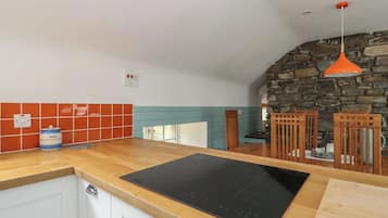 A kitchen with a black induction cooktop, wooden cabinets, a stone wall, and a hanging orange pendant light.