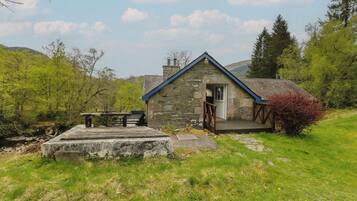 A stone cottage with a wooden deck, a bench, and a small table.
