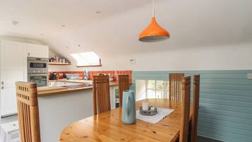 A modern kitchen with a dining area, featuring a wooden table, chairs, and a hanging orange pendant light.