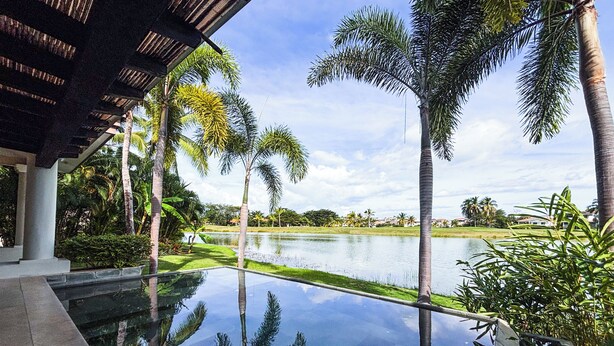 A swimming pool with a clear view of the surrounding landscape, including palm trees and a distant body of water. - Splendid 4BR Villa at Buenaventura Resort (Río Hato)