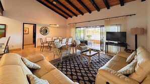 A spacious living room with a high ceiling, a dining area with chairs, a sofa set, a television, and a lamp. - Splendid 4BR Villa at Buenaventura Resort (Río Hato)