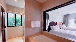 A hotel room with a large bed, a bathtub, a window with blinds, and a view of greenery outside. - Splendid 4BR Villa at Buenaventura Resort (Río Hato)