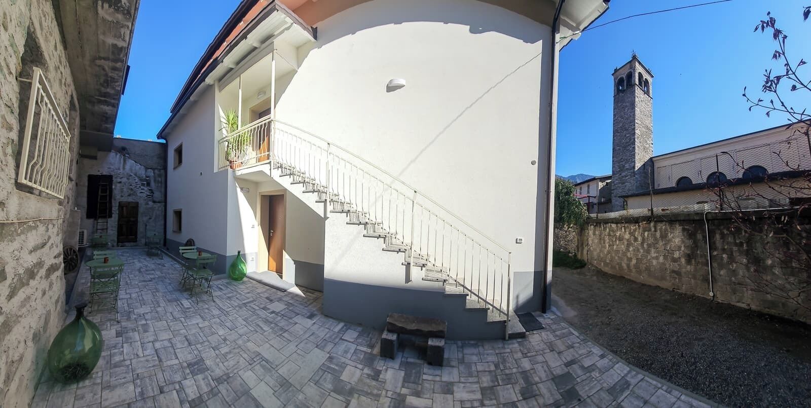 A courtyard with a white building, a staircase, and a stone wall.