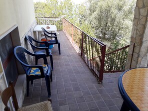 Un balcon avec une table et des chaises, un mur en pierre et une vue sur les arbres.