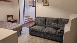 Una habitación con un sofá estampado, una cama con ropa de cama a rayas, una silla de madera y una escalera que sube a un nivel superior.