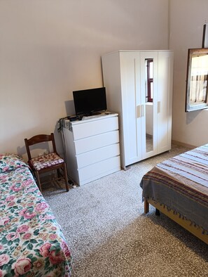 Ein Schlafzimmer mit Bett, Stuhl, Kleiderschrank und Fernseher auf einer Kommode.