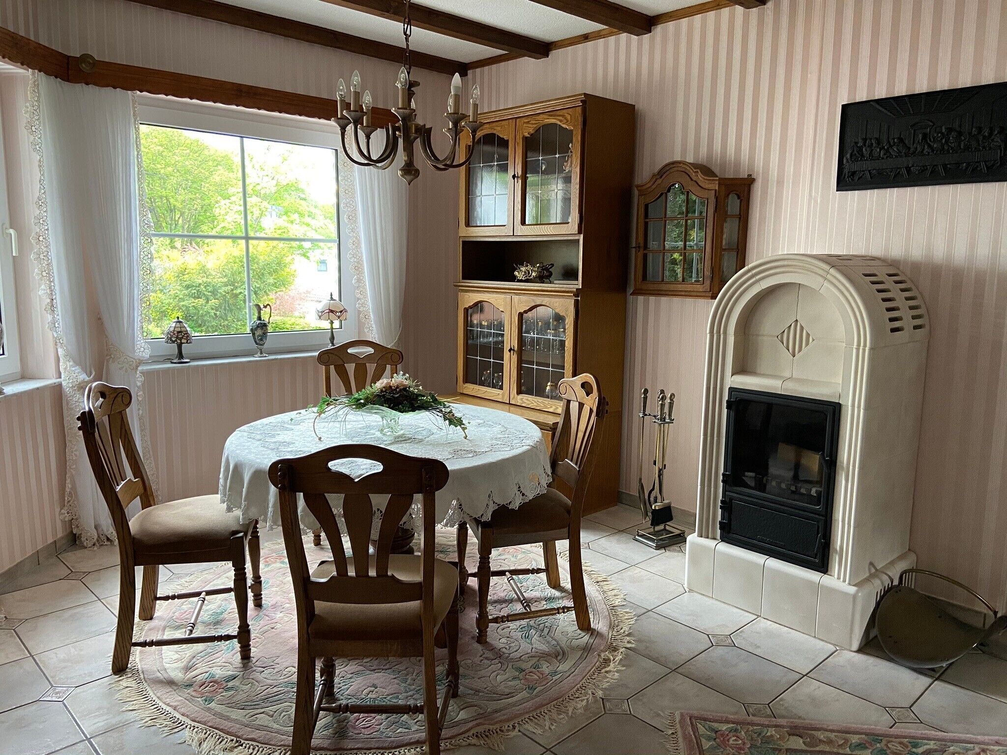 Une salle à manger avec une table ronde, quatre chaises en bois, un lustre, une cheminée et une fenêtre avec des rideaux.