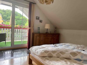 Un dormitorio con cama, un armario de madera, una lámpara y vistas a un balcón con flores.