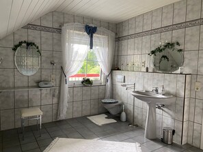 Baño con inodoro, lavabo y zona de ducha, con paredes de azulejos y una ventana con vistas.