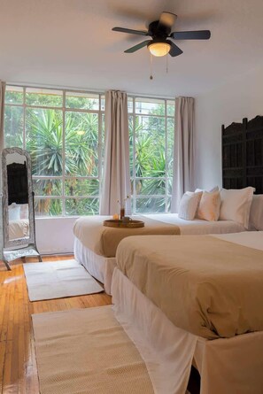 A bedroom with two beds, a ceiling fan, a large window with curtains, and a view of greenery outside. - Location- Design and Comfort Fully Equipped (Mexico City)