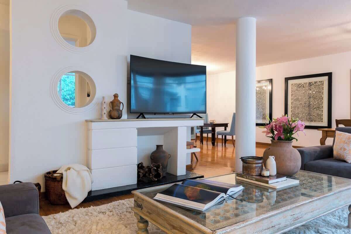 Ein modernes Wohnzimmer mit Flachbildfernseher, einem weißen Lowboard, einem Glastisch und einer Couch.