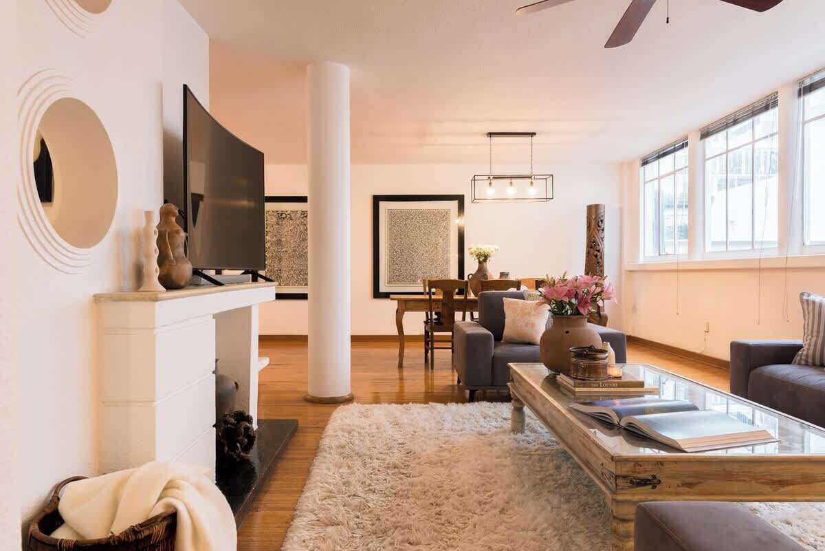 A modern living room with a fireplace, a television, a dining area, and a large window.