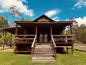 Eine rustikale Holzhütte mit Veranda und einer Treppe zum Eingang, der Himmel ist klar.