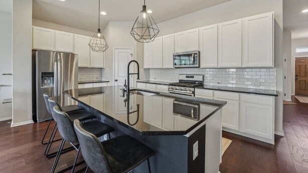 A modern kitchen with white cabinets, a stainless steel refrigerator, a built-in oven, and a large island with bar stools. - Adorable 3-bedroom Basecamp ATX (Buda)