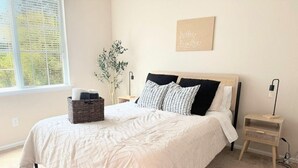 A bedroom with a bed, a bedside table, a lamp, a wall art piece, and a window with a view. - Adorable 3-bedroom Basecamp ATX (Buda)