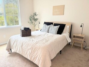 A bedroom with a bed, a bedside table, a lamp, a wall art piece, and a window with a view. - Adorable 3-bedroom Basecamp ATX (Buda)
