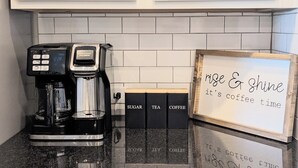 A coffee maker on a countertop with a sign that reads 'rise & shine it's coffee time' and labeled boxes for sugar, tea, and coffee. - Adorable 3-bedroom Basecamp ATX (Buda)