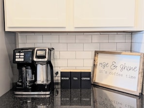 A coffee maker on a countertop with a sign that reads 'rise & shine it's coffee time' and labeled boxes for sugar, tea, and coffee. - Adorable 3-bedroom Basecamp ATX (Buda)