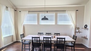A dining area with a long table and chairs, large windows with blinds, and a pendant light. - Adorable 3-bedroom Basecamp ATX (Buda)