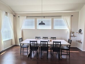 A dining area with a long table and chairs, large windows with blinds, and a pendant light. - Adorable 3-bedroom Basecamp ATX (Buda)
