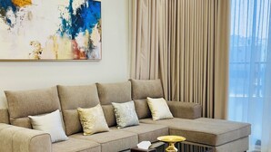 A modern living room with a sectional sofa, a glass coffee table, and a large abstract painting on the wall. - LAVIN SUITES SERVICED APARTMENTS  (At Taif)