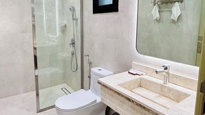 A modern bathroom with a glass shower enclosure, a toilet, a sink with a mirror, and a towel rack. - LAVIN SUITES SERVICED APARTMENTS  (At Taif)