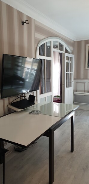 Ein Zimmer mit Fernseher auf einem Schrank, einem Glastisch, einem weißen Kleiderschrank mit Glastüren und einer weißen Decke.