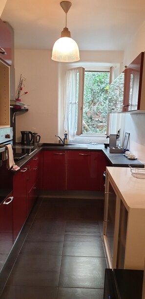 Eine Küche mit roten Schränken, einer schwarzen Arbeitsplatte, einem Fenster mit Vorhängen und einer Pendelleuchte.