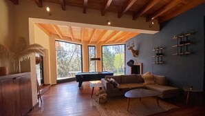 A spacious living room with wooden floors, a pool table, a sofa, and a large window offering a view of trees. - CABAÑA RANCHO SAN FRANCISCO TAPALPA (Tapalpa)