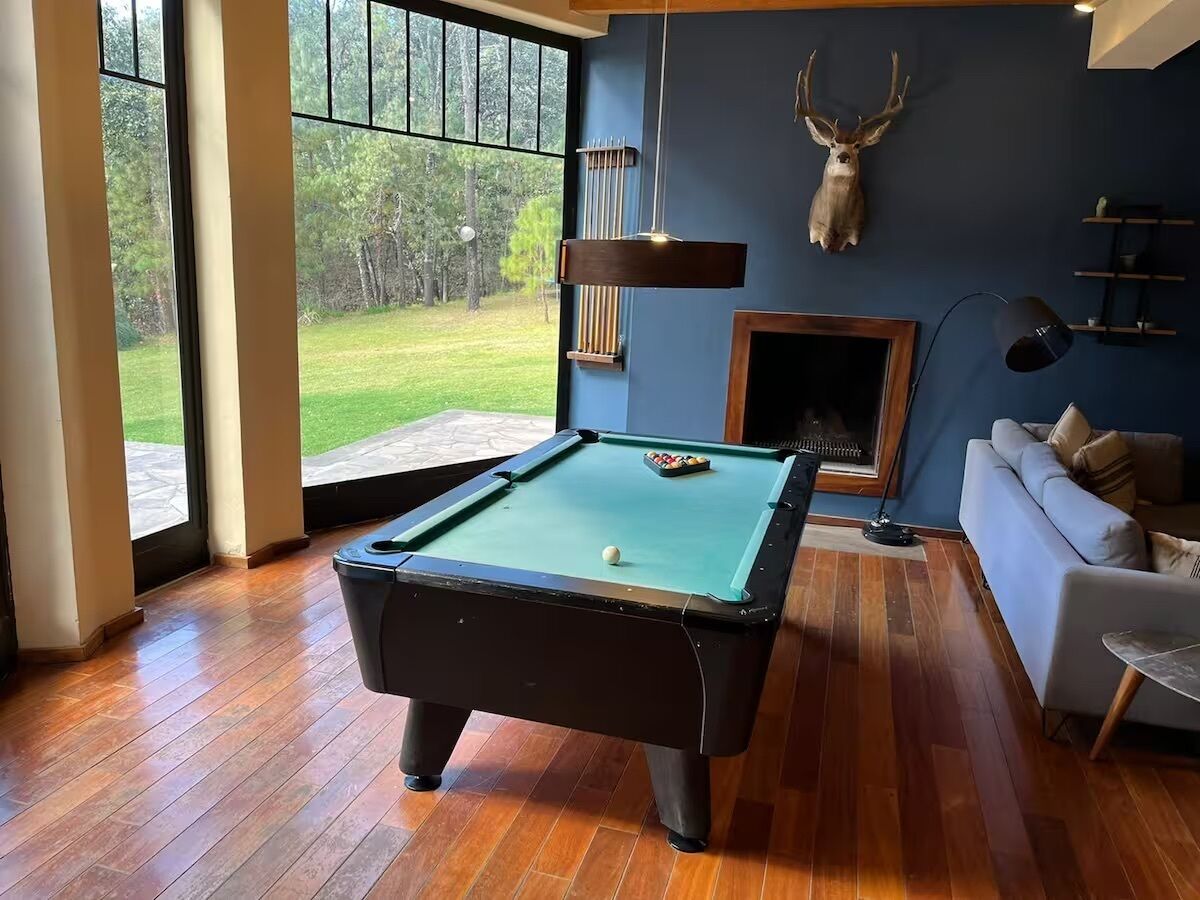 A pool table in a room with a fireplace, a sofa, and a deer head mounted on the wall.
