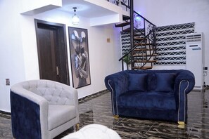 Ein modernes Wohnzimmer mit einem blauen Sofa, einem grauen Sessel, einer Treppe und einer Wand mit Muster.