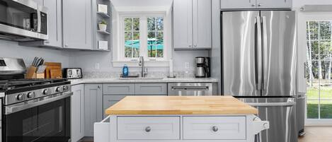 A modern kitchen with grey cabinets, a stainless steel refrigerator, a built-in oven, and a wooden countertop.